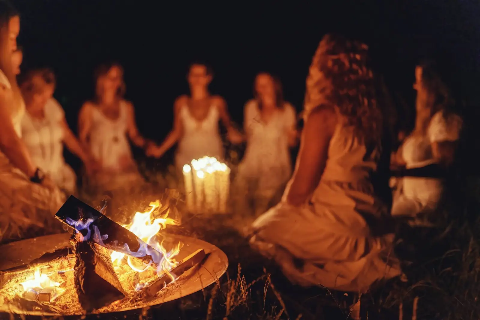 Frauen sitzen abends im Kreis um ein Feuer