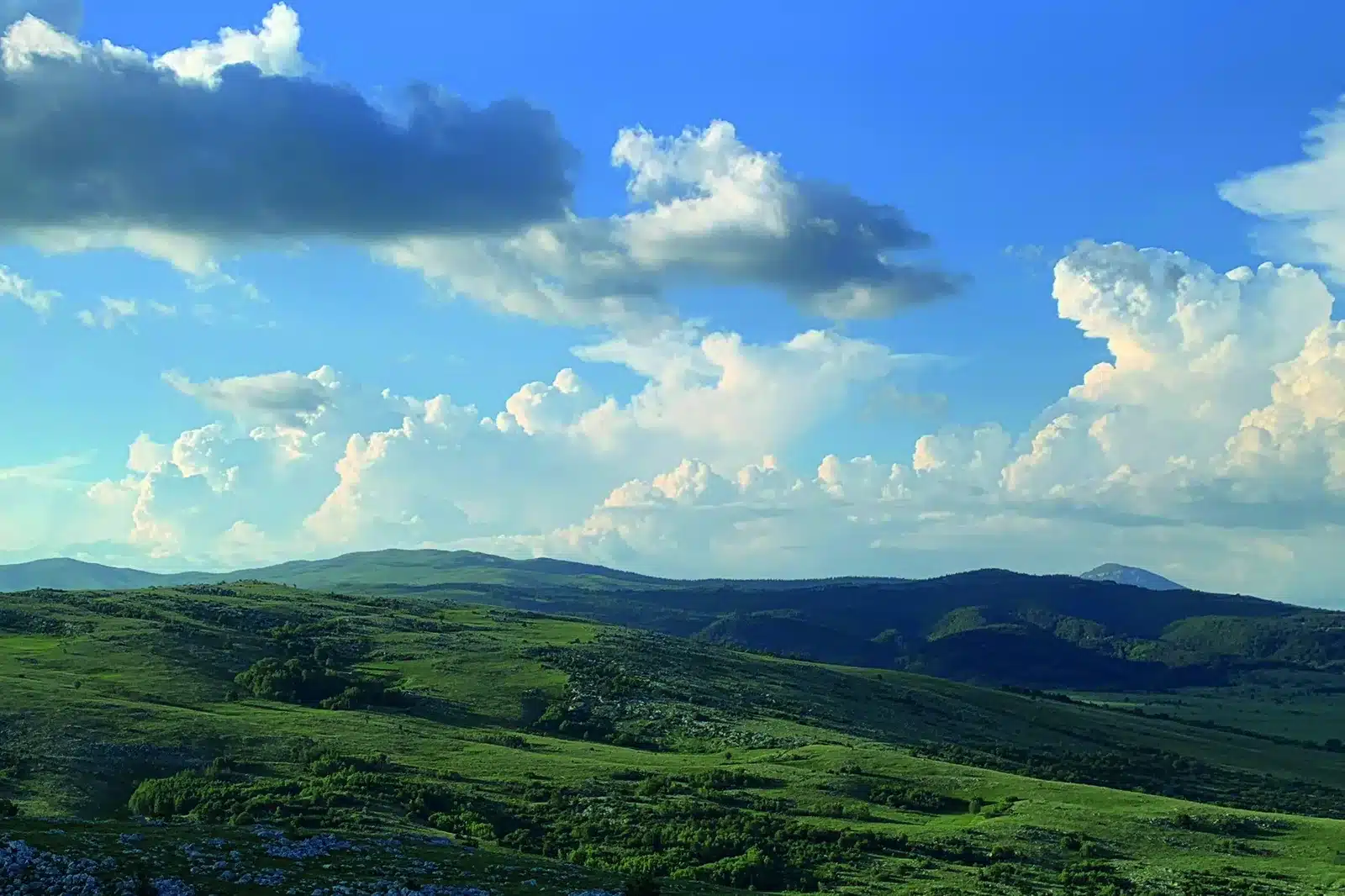 Weite grüne Hügellandschaft unter blauem Himmel mit Wolken